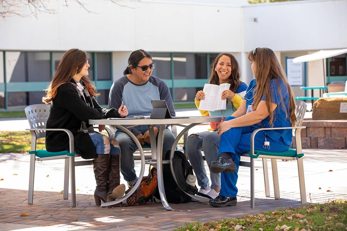 Four 十大电子游艺 students sitting at a table outside conversing and smiling.